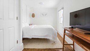 Une chambre à coucher avec un lit, un bureau en bois, une télévision et une fenêtre.