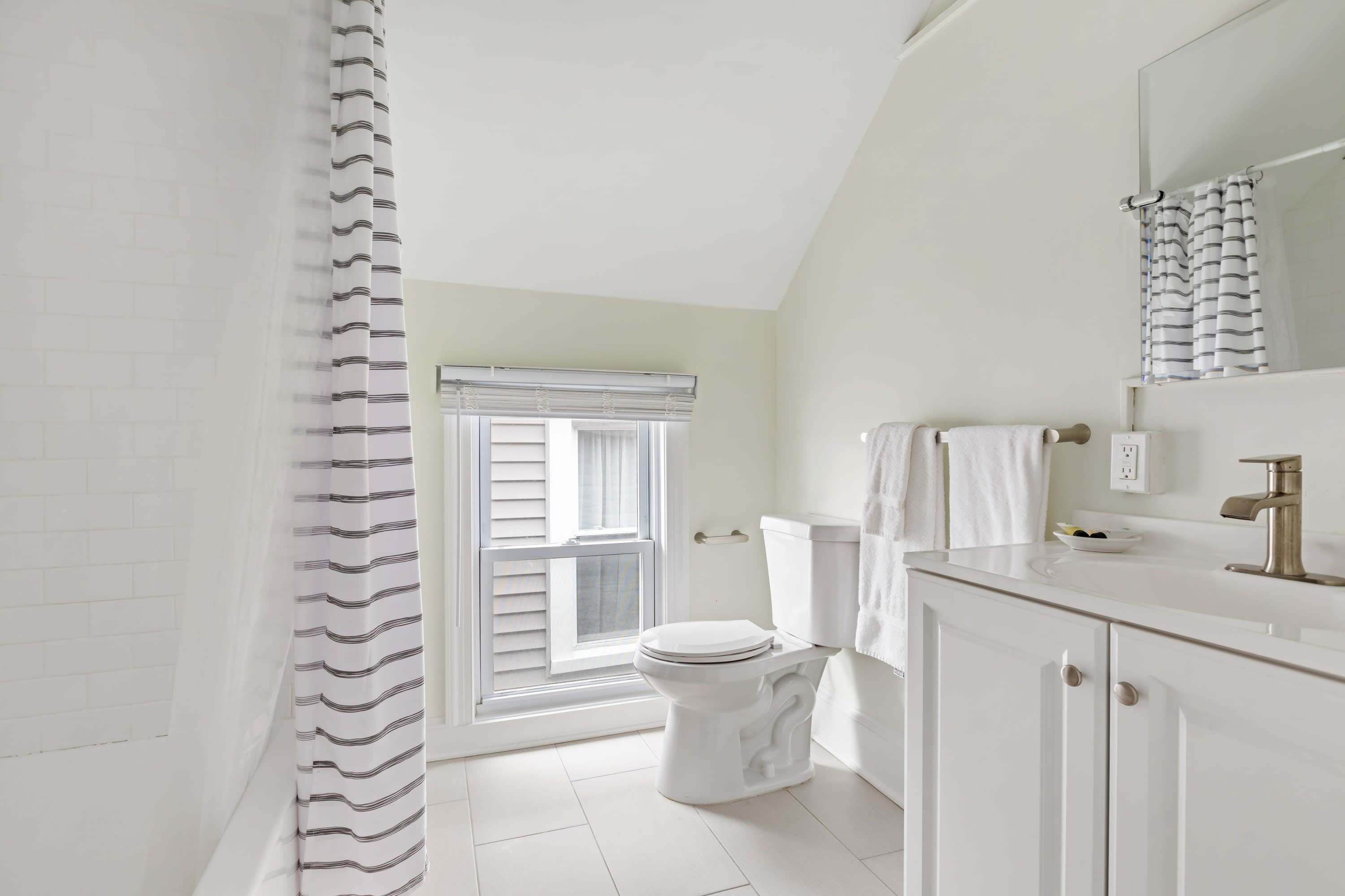A bathroom with a toilet, sink, and window with blinds.