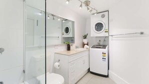 A modern bathroom with a glass shower enclosure, a toilet, a sink with a mirror, and a built-in washing machine.