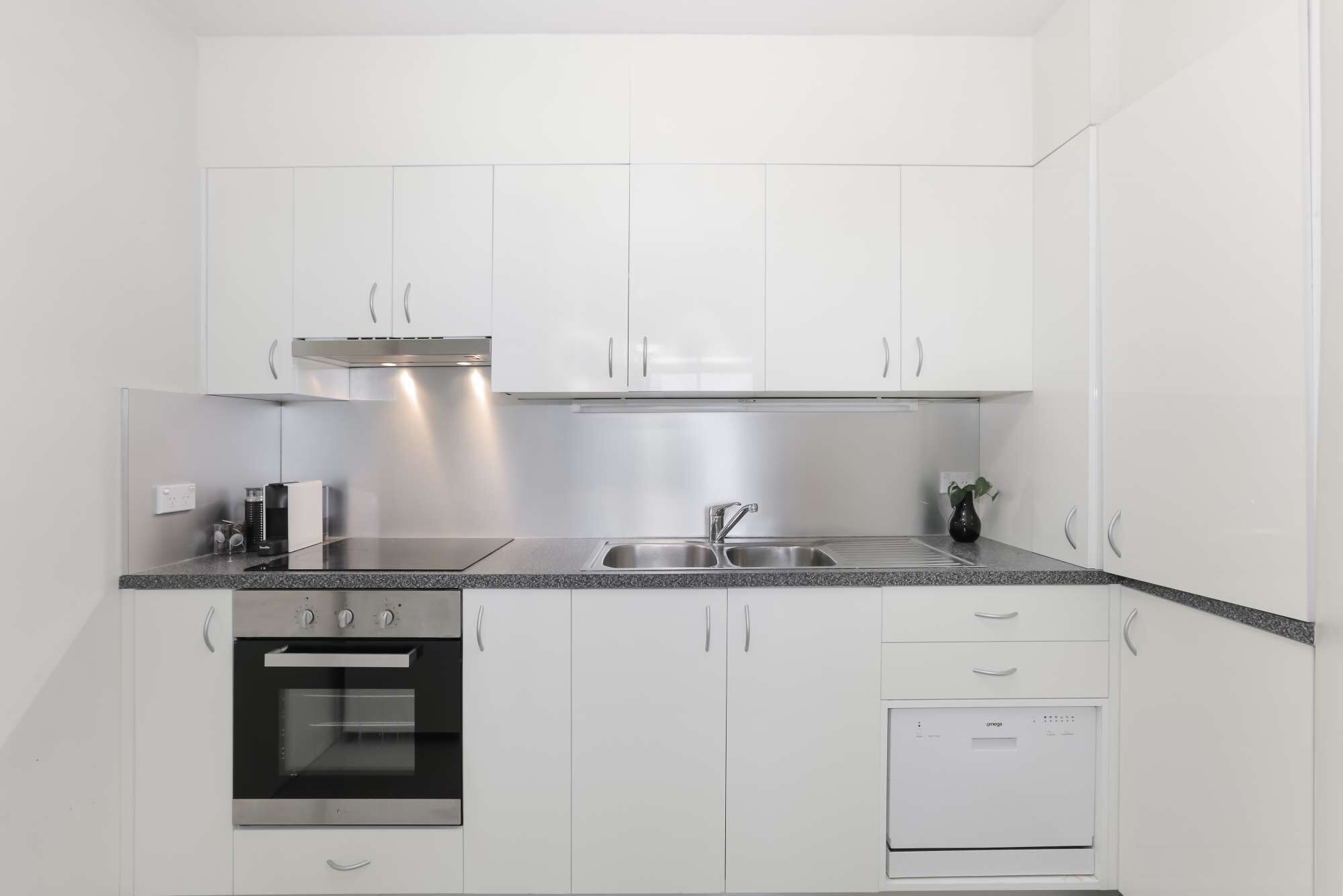 A modern kitchen with white cabinets, a stainless steel range hood, a double sink, an oven, and a dishwasher.