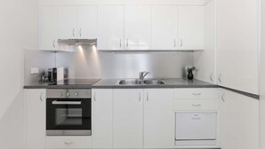 A modern kitchen with white cabinets, a stainless steel range hood, a double sink, an oven, and a dishwasher.