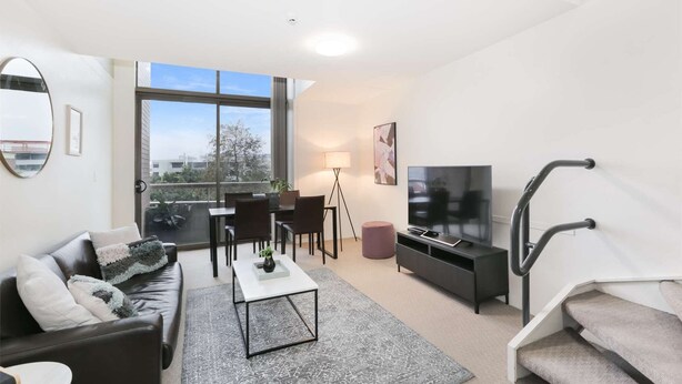 A modern living room with a sofa, coffee table, TV, and a dining area with chairs and a table.