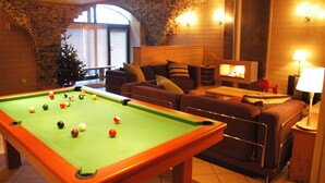 Een pooltafel in een ruimte met een stenen muur, een open haard en een bank met kussens.