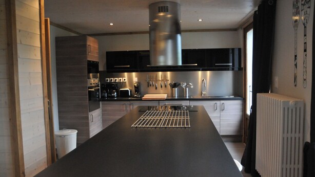 A modern kitchen with a central island, stainless steel appliances, and black cabinetry.