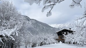 A wooden cabin with a balcony, surrounded by snow-covered trees and mountains in the background.