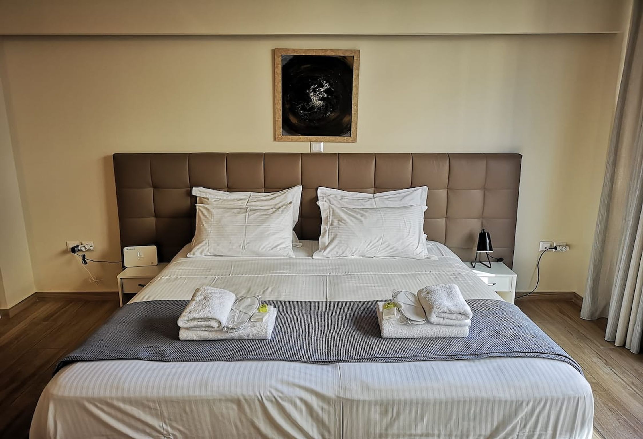 A neatly made bed with white linens and two pillows, a bedside table with a lamp, and a framed artwork on the wall.