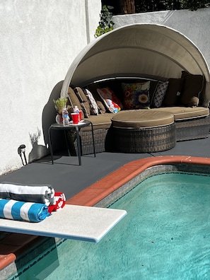 A poolside area with a covered seating area, a table with drinks, and a pool with a diving board. - Pool Guesthouse near Hollywood & Studios (Burbank)