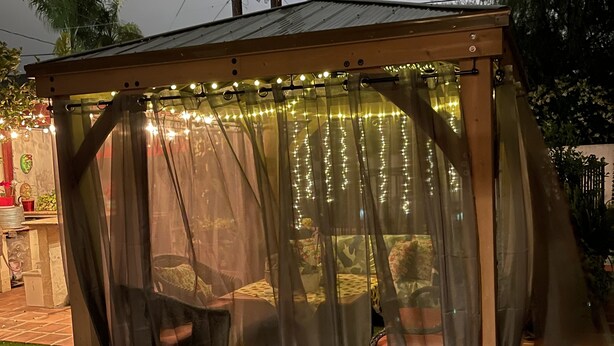 A covered outdoor seating area with a canopy, artificial grass, and string lights. - Pool Guesthouse near Hollywood & Studios (Burbank)