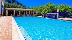 A clear blue swimming pool with a covered seating area and a waterfall feature.