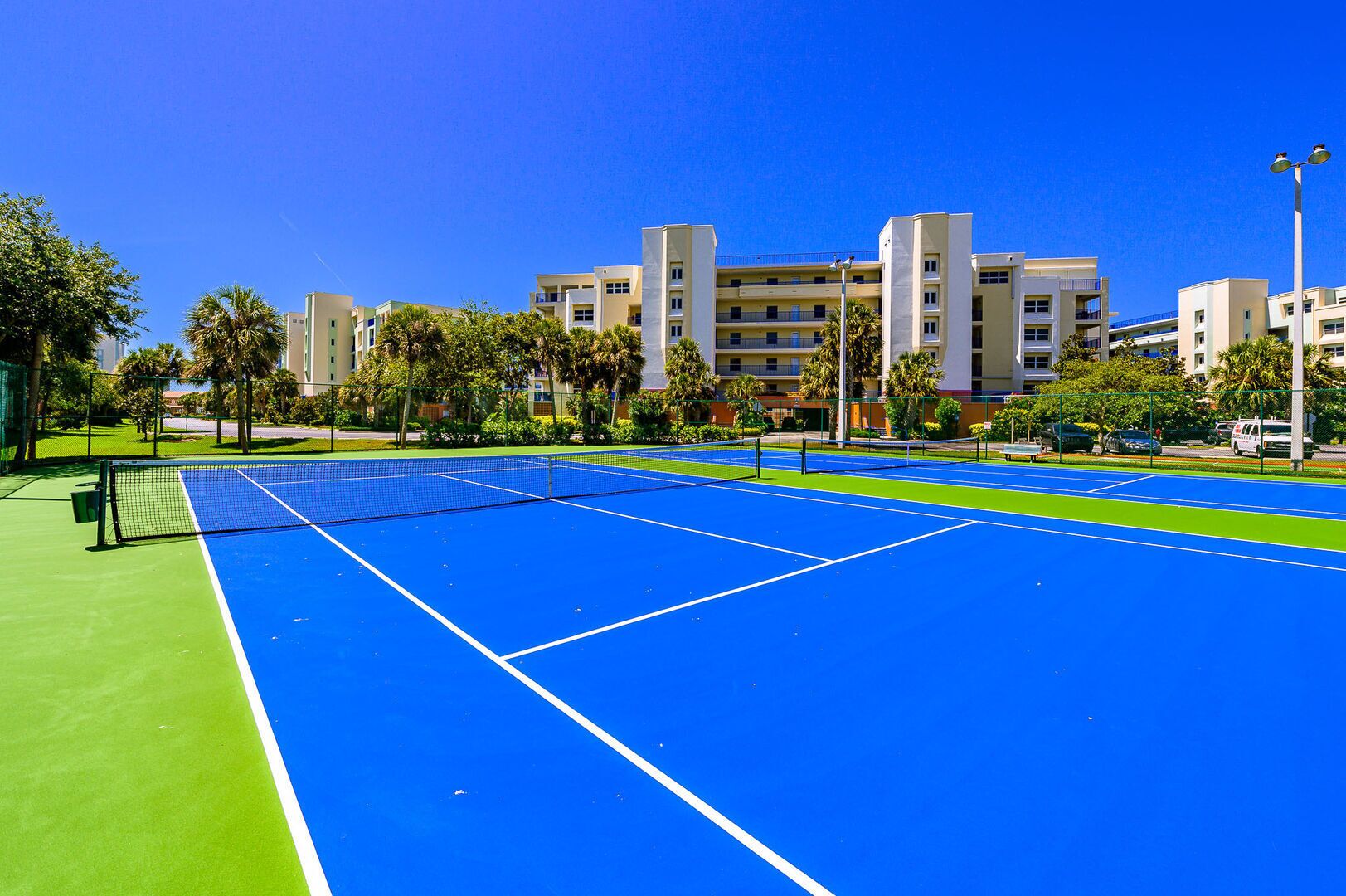 Un court de tennis avec un filet, entouré d’une clôture et de palmiers.