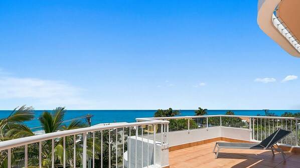 A balcony with a view of the ocean, a chair, and a railing.