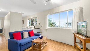 A living room with a blue sofa, a wooden coffee table, a television on a wooden stand, and a large window with curtains.