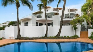 A modern multi-story building with balconies, a swimming pool, and palm trees.
