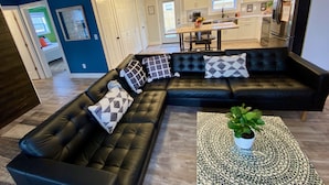 Un salon moderne avec un canapé d’angle en cuir noir, une table basse surmontée d’un plateau en mosaïque et une plante en pot.