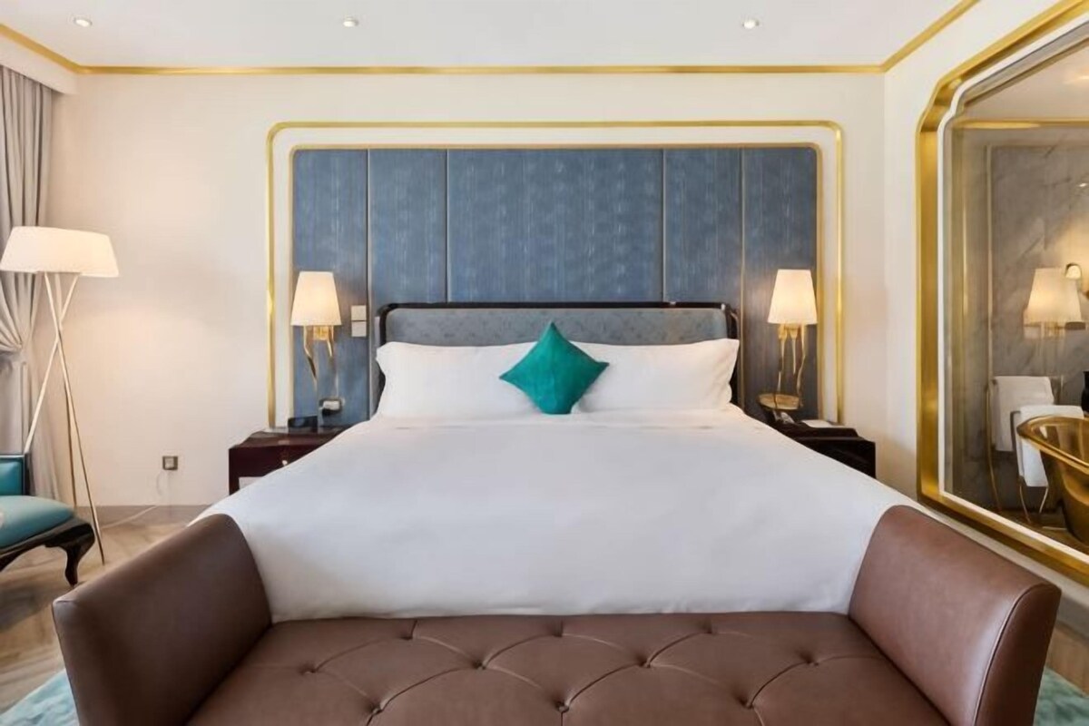 Una habitación de hotel con una cama grande, cabecera tapizada, dos lámparas de noche y un espejo amplio.