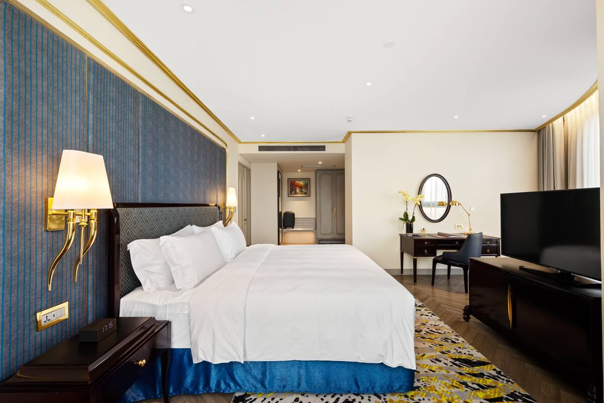 A hotel room with a large bed, a desk with a chair, a television, and a mirror.