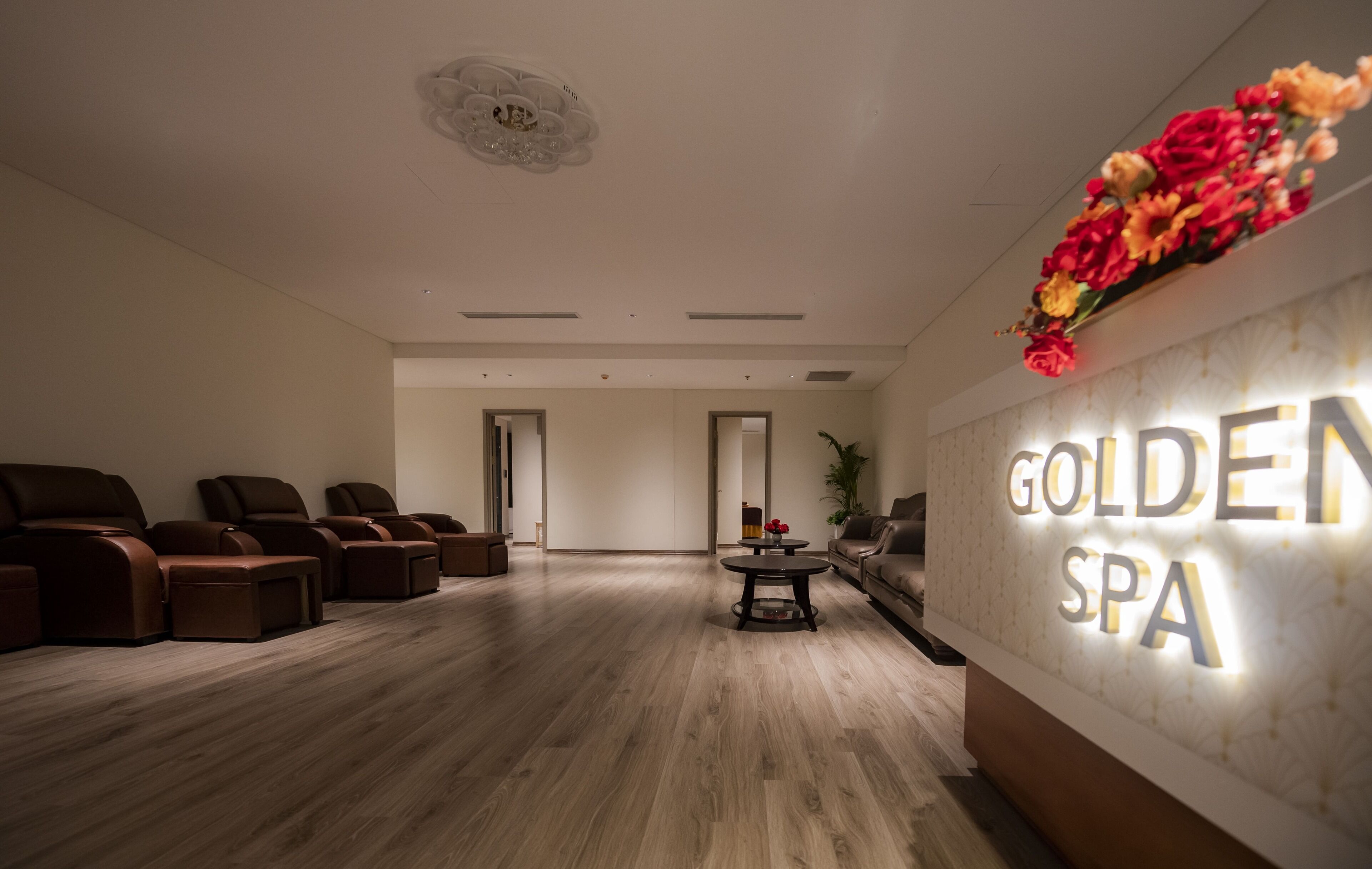 Zona de recepción de un spa, con suelo de madera, varias sillas de masaje, un mostrador de recepción y un letrero en la pared que dice 'GOLDEN SPA'.