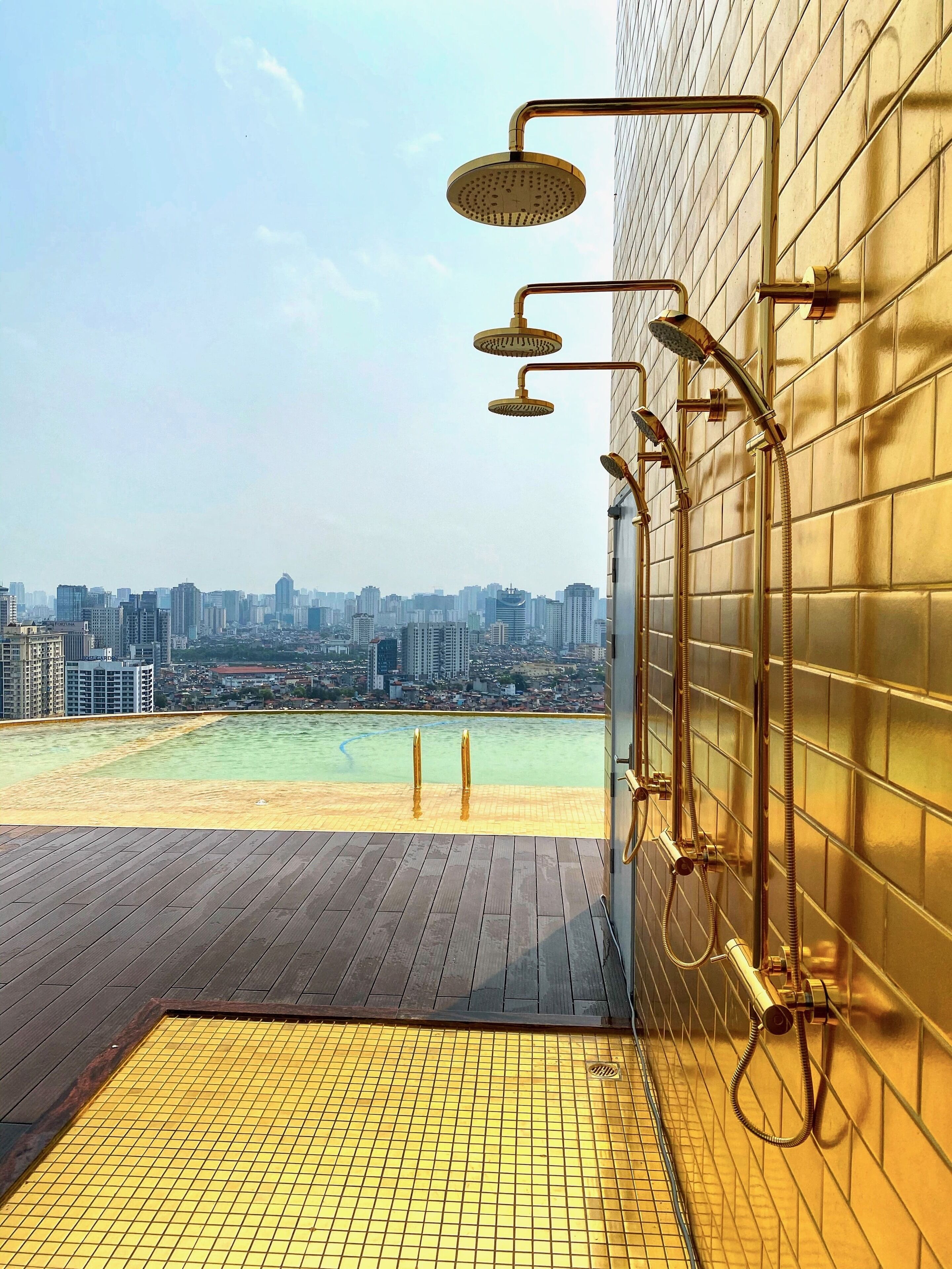Piscina no terraço com vista para a cidade, chão em mosaico e área de chuveiro com vários jatos.