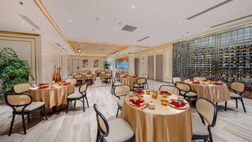 A spacious banquet hall with multiple round tables set for dining, surrounded by comfortable chairs.