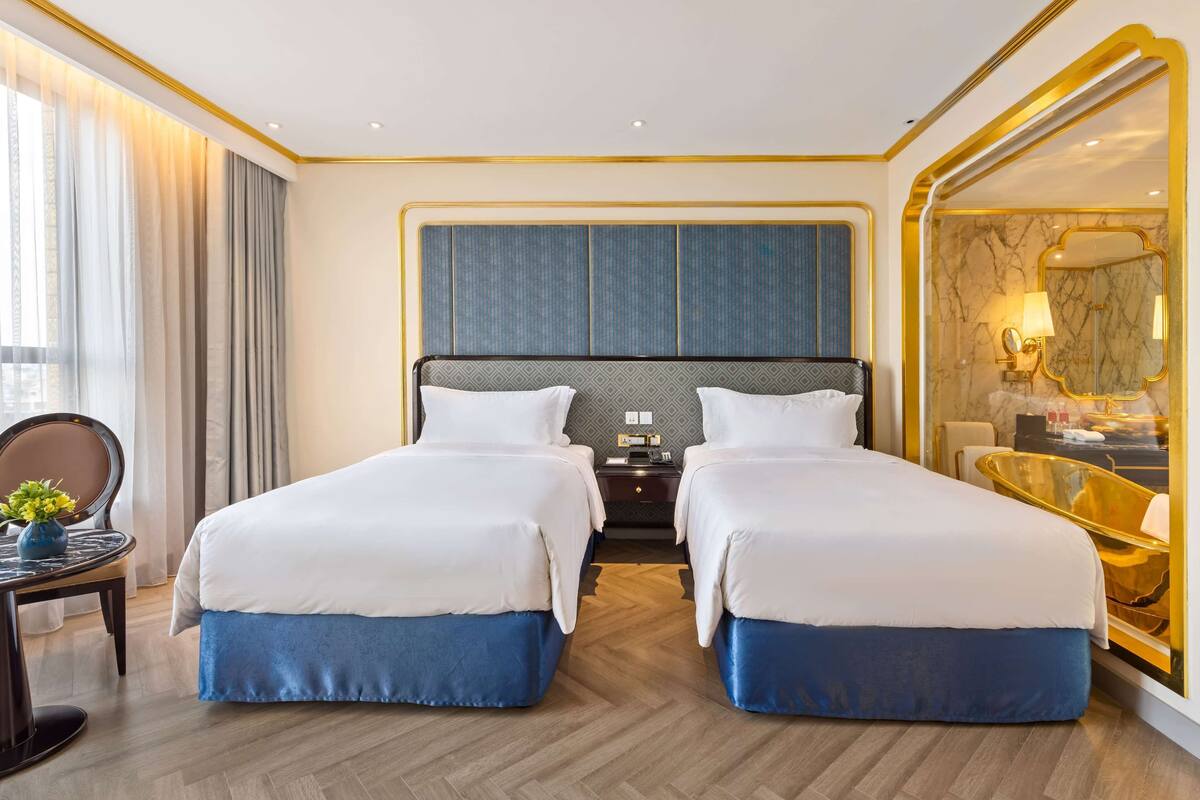 A hotel room with two beds, a desk, a chair, a mirror, and a view of the city.