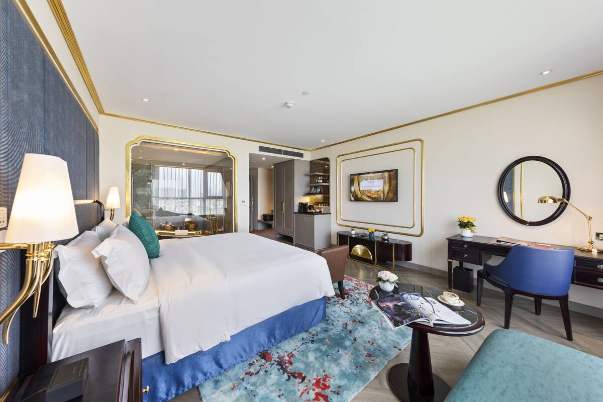 A modern hotel room with a large bed, a desk, a chair, and a television.