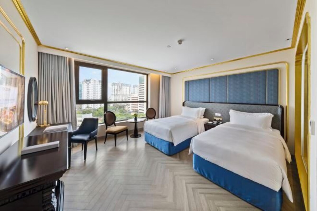 Habitación de hotel con dos camas, un escritorio, una silla, un televisor y vistas a la ciudad.