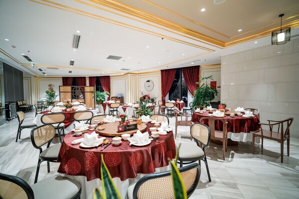 A spacious dining area with round tables, red tablecloths, and white chairs.