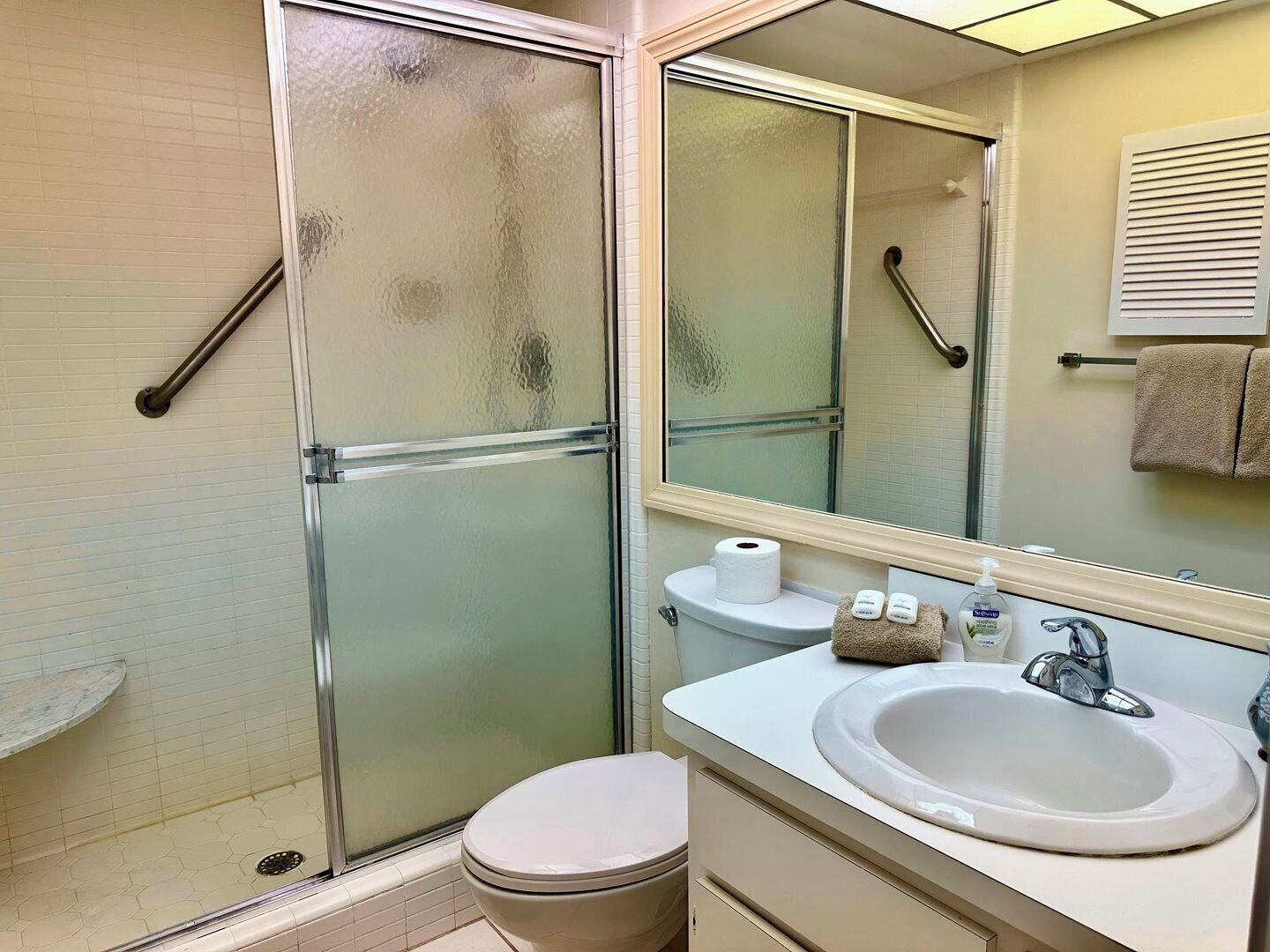 Une salle de bain avec une douche à parois de verre, des toilettes, un lavabo avec un miroir et un porte-serviettes.