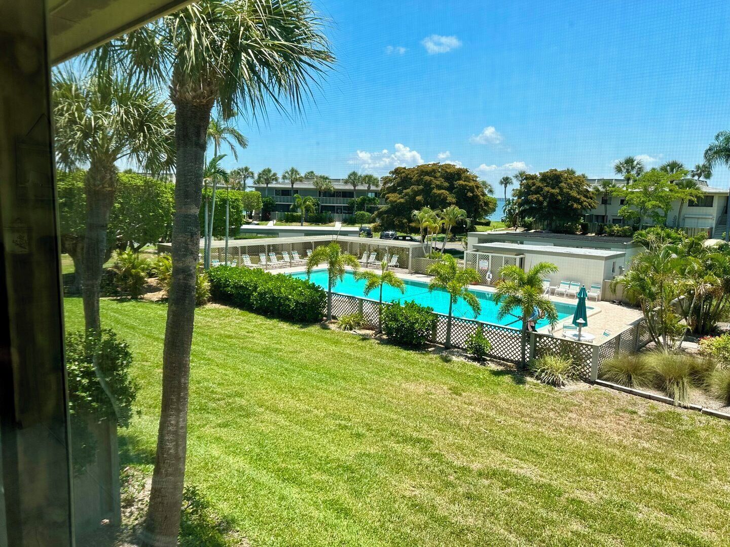 A pool area with a clear view of the pool, lounge chairs, and surrounding greenery.