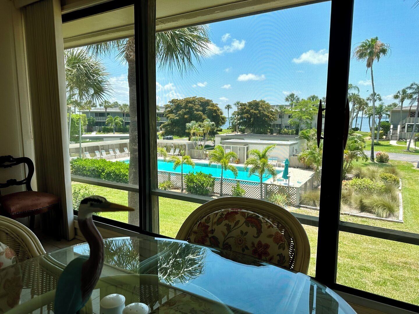 Habitación con vista a una piscina, mobiliario exterior y una silla con cojín floral.