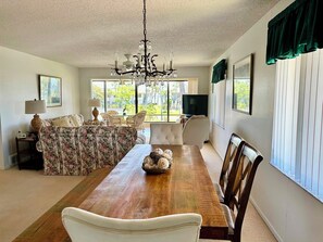 Uma sala de estar ampla com uma mesa de jantar de madeira, sofá floral e um lustre.