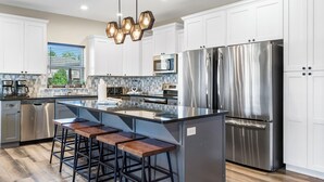 A modern kitchen with white cabinets, stainless steel appliances, a central island with bar stools, and a decorative hexagonal light fixture. - Breathtaking Home! *In Town*Fire-Pits* Indoor Pool*Yard Games*Golf View* (Branson)