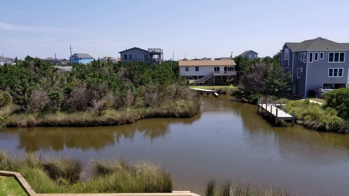 A calm river with a bridge, surrounded by residential buildings and dense greenery.