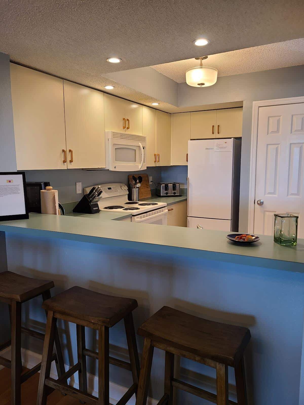 A kitchen with white cabinets, a microwave, a refrigerator, a stove, and a bar area with stools.