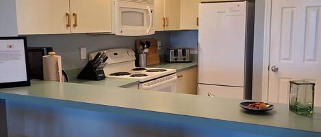 A kitchen with white cabinets, a microwave, a refrigerator, a stove, and a bar area with stools.