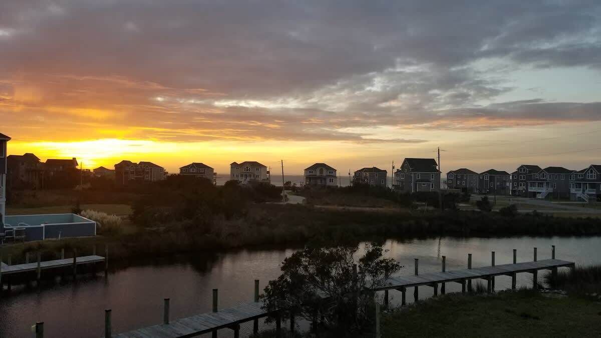 A waterfront residential area with houses, a dock, and a sunset.