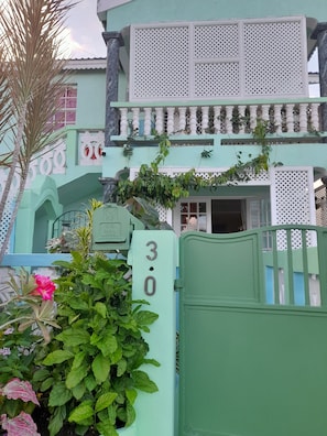 Un edificio de dos pisos con fachada verde, barandillas de celosía blancas y un portón verde con el número 30.