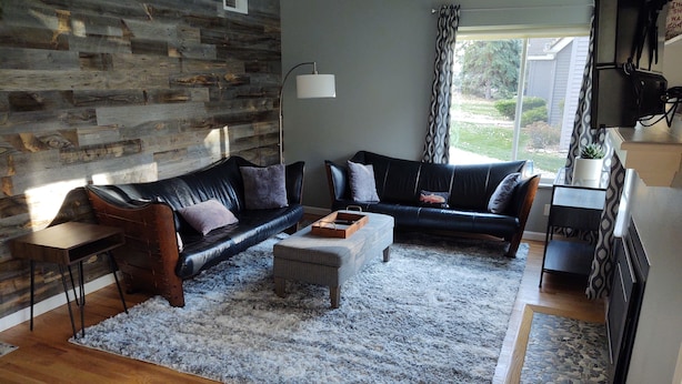 Ein Wohnzimmer mit einer Steinwand, zwei schwarzen Ledersofas, einem Holztisch und einem gemusterten Teppich.