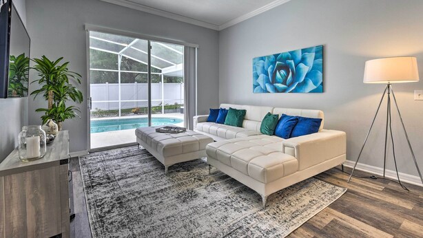 A modern living room with a white sofa, a coffee table, and a large window overlooking a pool.