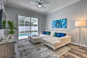 Una sala de estar moderna con un sofá blanco, una mesa de centro y un ventanal con vistas a una piscina.