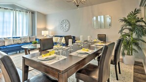 A dining area with a wooden table set for six, a chandelier, a clock, and a large mirror on the wall.