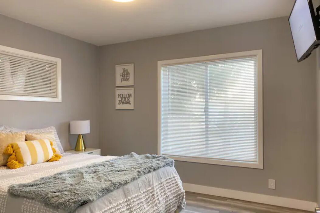 A bedroom with a bed, a window with blinds, a lamp, and wall art.