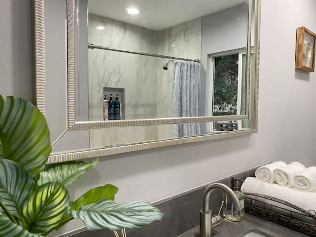 A bathroom with a large mirror, a towel rack with neatly folded towels, a shower curtain, and a potted plant.