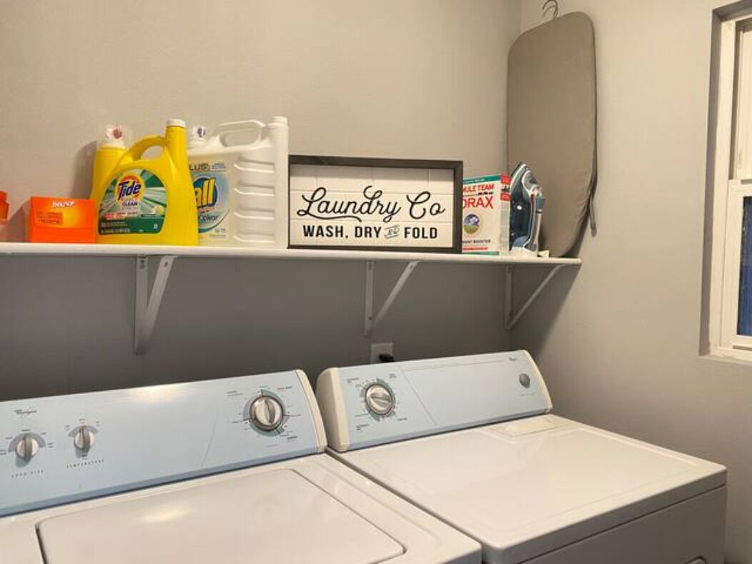 A laundry area with two front-loading washers, a shelf with laundry supplies, and a sign indicating the services offered.