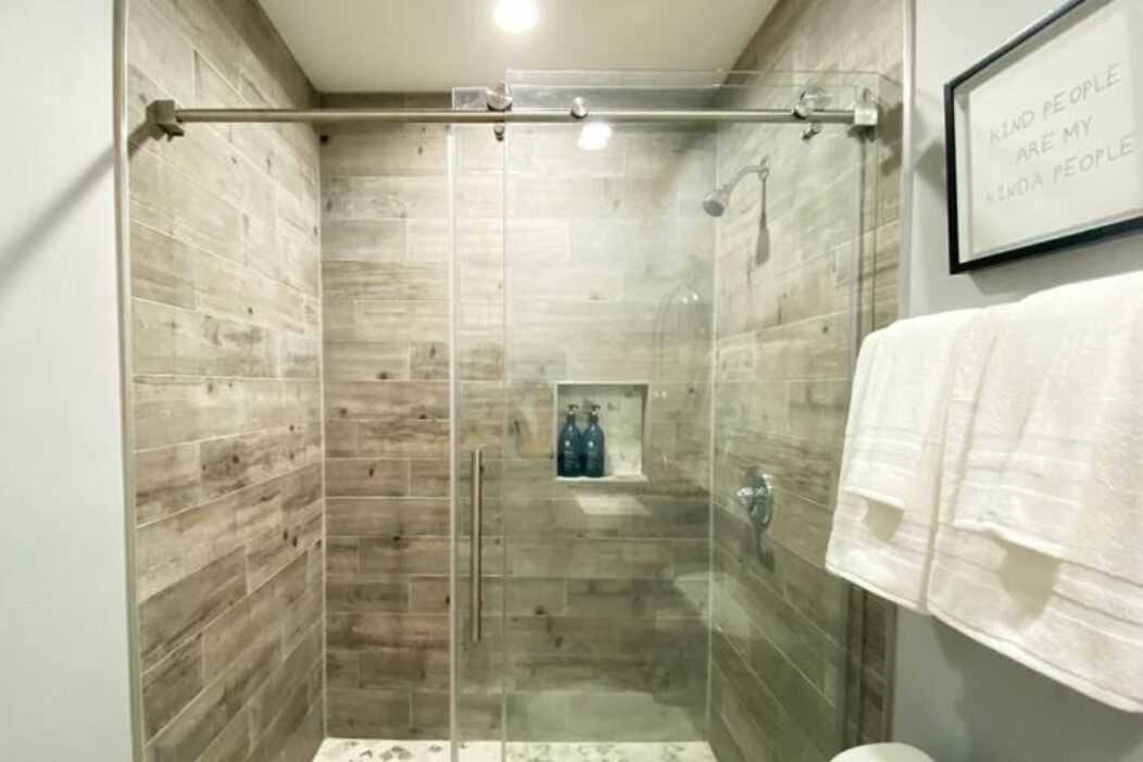 A glass-enclosed shower stall with a wooden wall design, a towel rack, and a framed quote on the wall.