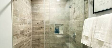 A glass-enclosed shower stall with a wooden wall design, a towel rack, and a framed quote on the wall.