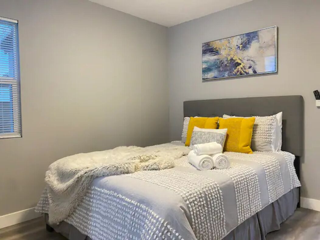 A bedroom with a bed, a painting, and a window with blinds.