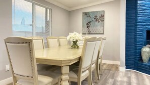 Une salle à manger avec une table beige et des chaises assorties, un vase de fleurs blanches et un mur d’accent bleu.