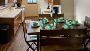 A spacious kitchen with wooden cabinets, a dining table set with green plates, and a hanging light fixture. - On the Rio Grande. Direct ATV Access from the property to National Forest Roads. (South Fork)