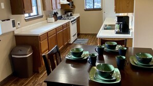 A compact kitchen with wooden cabinets, a dining table set with green plates, and a window providing natural light. - On the Rio Grande. Direct ATV Access from the property to National Forest Roads. (South Fork)